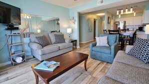 A living room with a sofa, armchair, coffee table, and a dining area with a table and chairs. - Compass Point 205 (Gulf Shores)