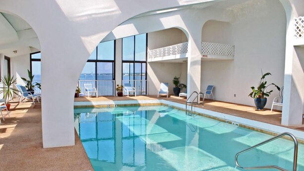 An indoor swimming pool with clear blue water, surrounded by white walls and large windows. - Compass Point 205 (Gulf Shores)