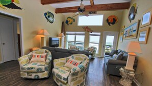 A living room with a sofa, two armchairs, a coffee table, and a TV. There are decorative fish on the walls and a ceiling fan. - Cabana Beach House (Gulf Shores)