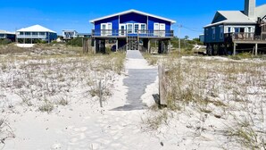 A beachfront property with a central house featuring a balcony and a covered walkway leading to it. - Cabana Beach House (Gulf Shores)
