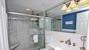 A modern bathroom with a glass-enclosed shower, a white toilet, and a white sink with a mirror above it. - Broadmoor 304 (Orange Beach)