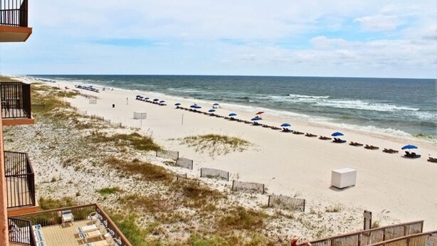 A beach with rows of umbrellas and lounge chairs, a wooden deck, and a view of the ocean. - Broadmoor 304 (Orange Beach)