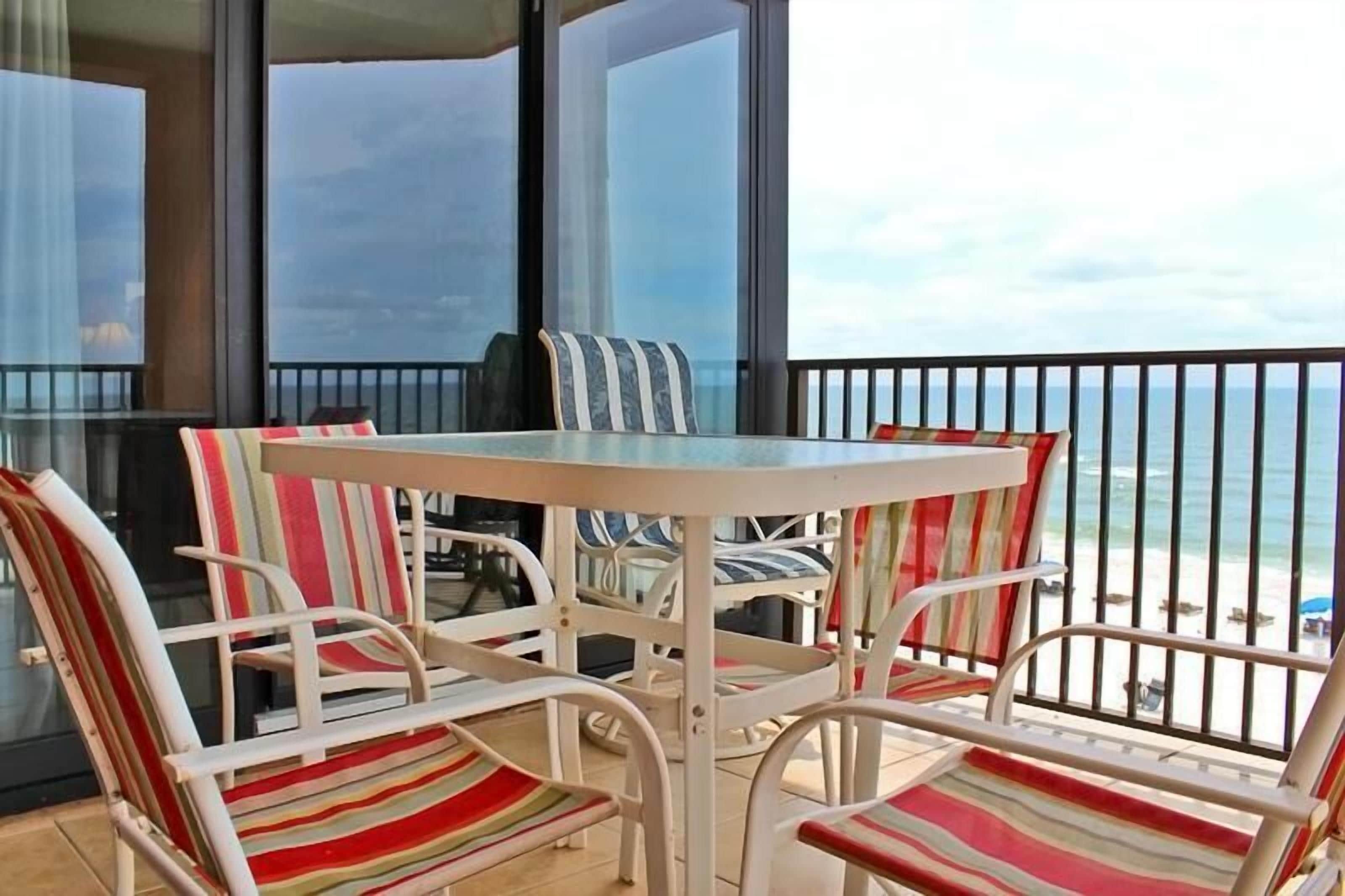 A balcony with a table and striped chairs, overlooking a beach.