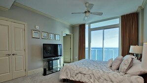Ein Hotelzimmer mit Bett, Fernseher, Deckenventilator und einem großen Fenster mit Blick auf den Ozean.