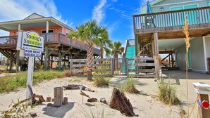 A beachfront property with a wooden deck, a sign advertising rental availability, and a building with a balcony. - Dream Catcher (Gulf Shores)
