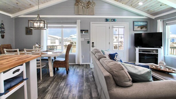 A spacious living area with a high ceiling, a dining table, a sofa, and a television. - Dream Catcher (Gulf Shores)
