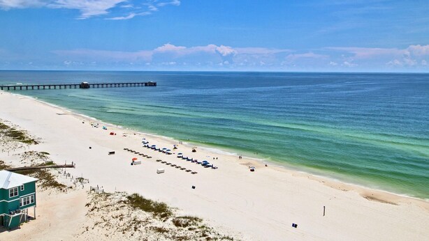 A beach with a pier extending into the ocean, a lifeguard tower, and several beach umbrellas. - Colonnades 1202 (Gulf Shores)