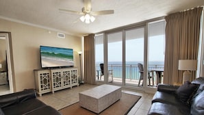 A living room with a flat-screen TV, leather sofas, a coffee table, and a balcony with a view of the ocean. - Colonnades 1202 (Gulf Shores)