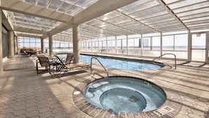 An indoor swimming pool with a glass ceiling, lounge area with chairs, and a view of the sea. - Colonnades 1202 (Gulf Shores)