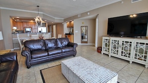 A living room with a leather sofa, a white coffee table, and a TV on a white cabinet. - Colonnades 1202 (Gulf Shores)