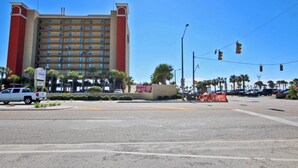 A multi-story hotel with a red and beige facade, located at a street intersection with traffic lights and palm trees. - Beachview 203 (Gulf Shores)