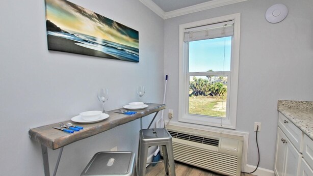 A kitchen with a window, a painting, and a table with two stools. - Beachview 203 (Gulf Shores)