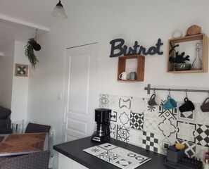 A kitchen with a coffee maker, a shelf with mugs, and a wall-mounted sign that reads 'Bistrot'.