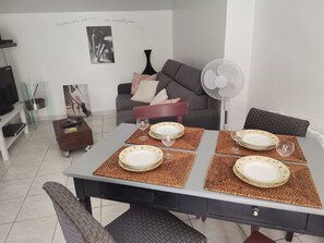 A dining area with a table set for four, a sofa, a TV, and a wall with a poster.