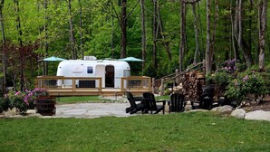 A mobile home with a covered porch and a deck, surrounded by a wooded area.