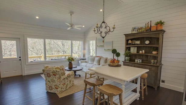A spacious living room with a white sofa, floral armchair, and a dining area with a white table and wooden stools.