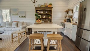 A kitchen with a central island, wooden stools, a white sofa, and a rustic wooden shelf with various items.