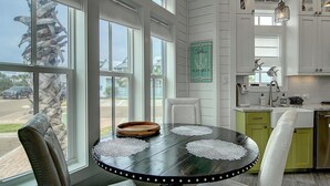 A kitchen with a round table, chairs, and a view of the street through large windows. - Stay@‘Summer Breeze,’ a 2-Story, Cinnamon Shore Townhome w/ Great Amenities (Port Aransas)