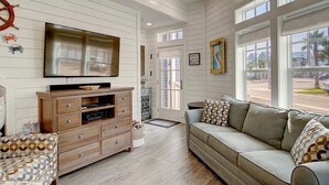 A living room with a TV, wooden entertainment center, and a sofa with patterned cushions. - Stay@‘Summer Breeze,’ a 2-Story, Cinnamon Shore Townhome w/ Great Amenities (Port Aransas)