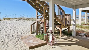 Eine hölzerne Strandpromenade mit Treppe und einer Holzterrasse, in der Nähe liegt eine aufgerollte Gartenschlauch.