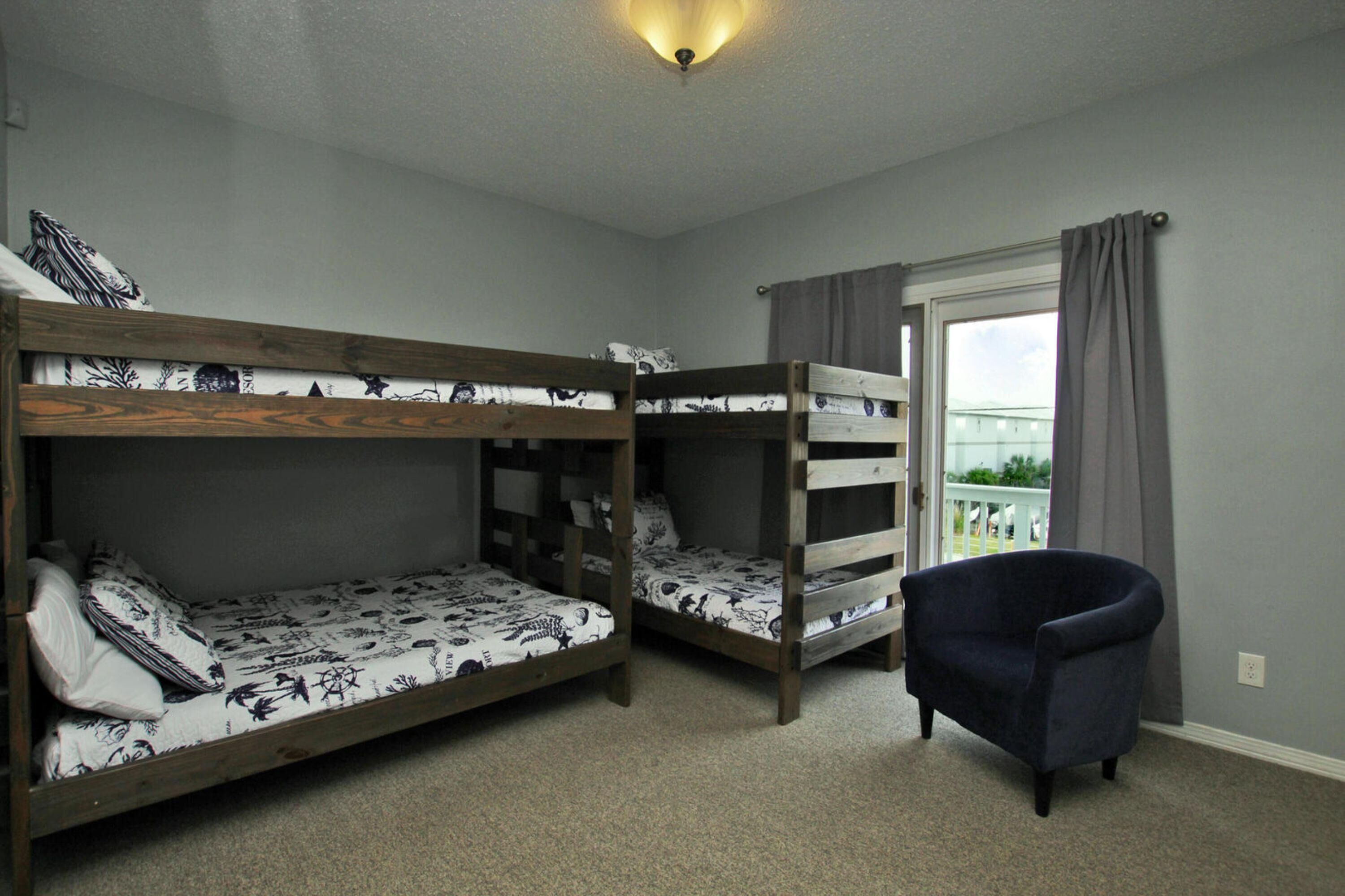 A room with bunk beds, a chair, and a window with curtains.