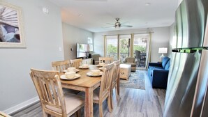 A dining area with a wooden table and chairs, a television, and a view of the outdoors. - Laguna Bella B1 (Gulf Shores)