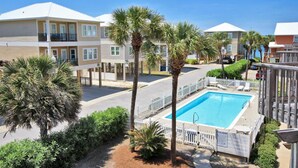 A hotel with a swimming pool surrounded by palm trees and a white fence. - Laguna Bella B1 (Gulf Shores)