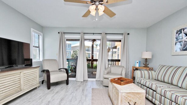 A living room with a television, two armchairs, a sofa, a coffee table, and a ceiling fan. - Laguna Bella B1 (Gulf Shores)