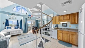 A spacious living area with a large bed, a staircase leading to an upper level, a kitchen with wooden cabinets, and a view of the sky through a skylight.