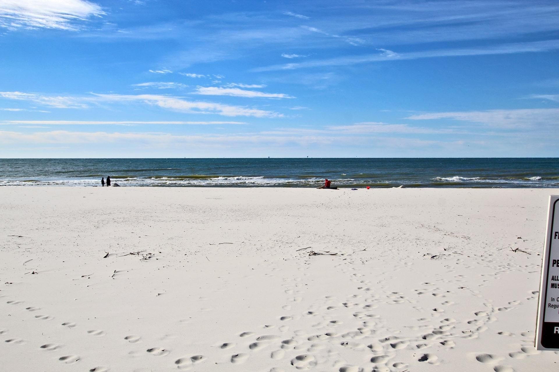 A beach with footprints leading to the water, a lifeguard tower, and a clear sky.