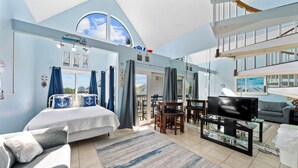 A spacious living area with a large bed, a television, and a balcony with a view.