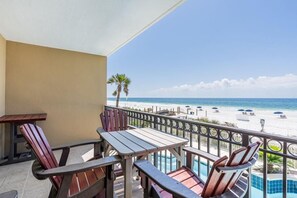 Un balcon avec des chaises et une table en bois, donnant sur une plage parsemée de parasols et de chaises longues.