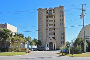 Un hôtel à plusieurs étages, doté d’une entrée centrale, entouré de palmiers et comprenant un espace de stationnement.