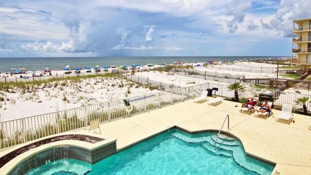 A pool area with a view of the beach and ocean, surrounded by lounge chairs and umbrellas. - Legacy 102 (Gulf Shores)