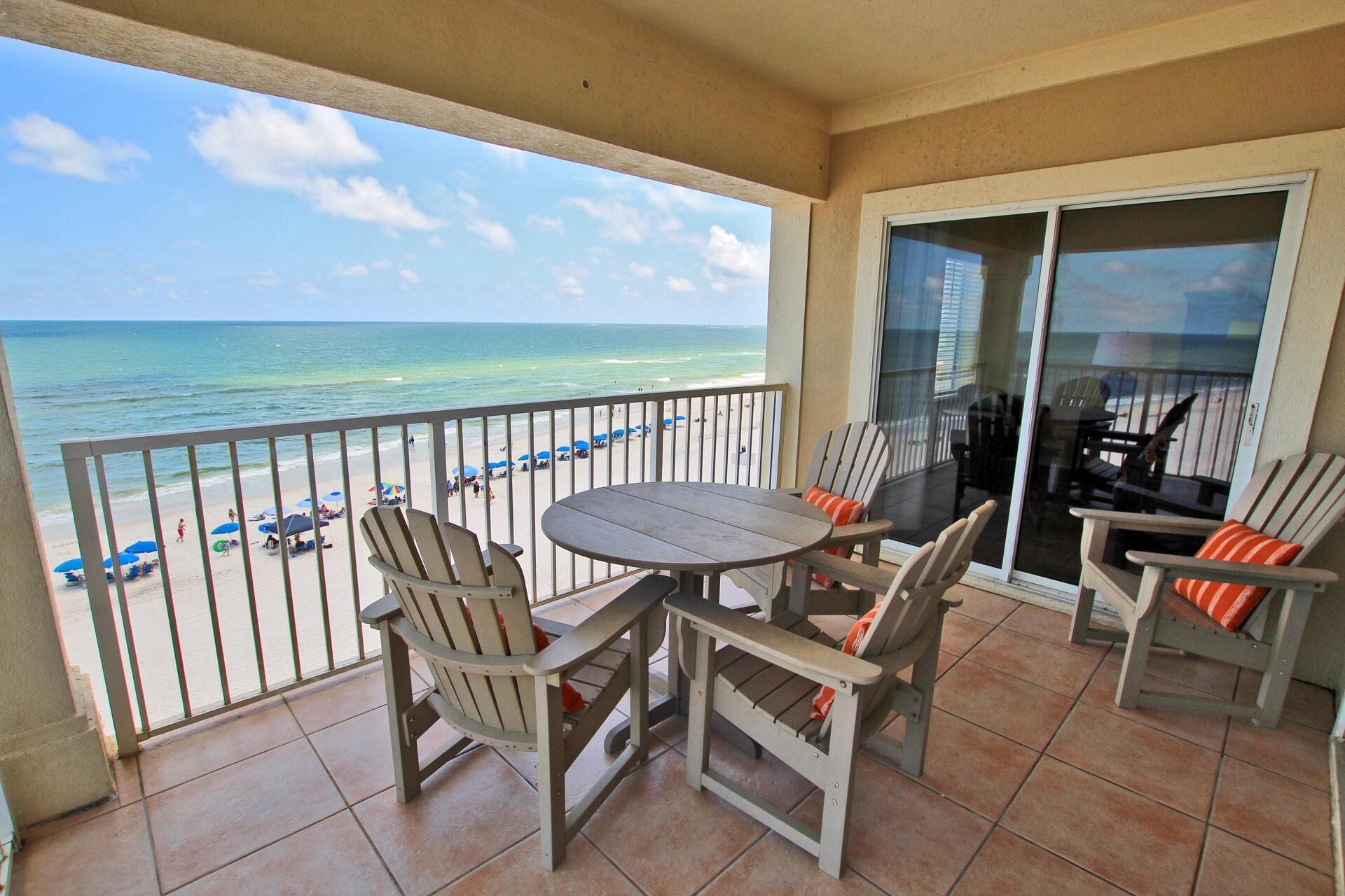 A balcony with a view of the beach, a round table, and two chairs.