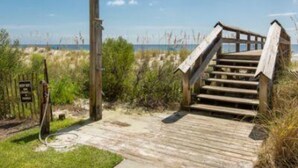 A wooden staircase leading to a beach area with a clear view of the ocean.