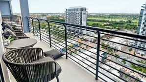 Ein Balkon mit Korbstühlen und einem Tisch, der einen Blick auf eine Stadt mit Gebäuden und Grünflächen bietet.