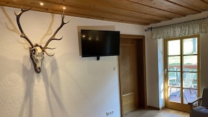 Une pièce décorée d’un trophée de tête de cerf accroché au mur, d’un téléviseur et d’une porte donnant sur un espace extérieur avec une terrasse.