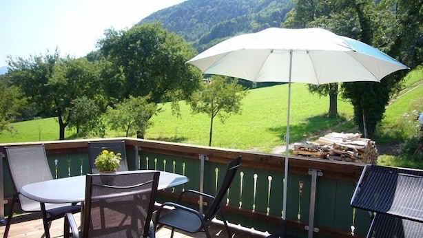 Une terrasse avec une table et des chaises, un parasol et une pile de bois de chauffage.