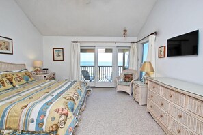 Une chambre à coucher comprenant un lit, une commode, une chaise, un téléviseur et une vue sur la mer, accessible par une porte coulissante.