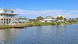 A waterfront property with a large house featuring a balcony and a dock extending into the water. - Sunset Daze (Gulf Shores)