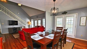 A dining area with a wooden table set for four, a red sofa, and a staircase in the background. - Sunset Daze (Gulf Shores)