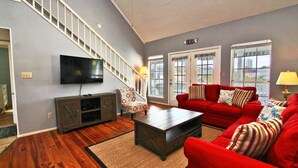 A spacious living room with a staircase, a flat-screen TV, a red sofa, and a patterned armchair. - Sunset Daze (Gulf Shores)
