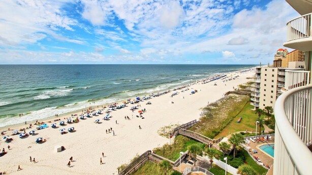 A beach view from a balcony overlooking a sandy beach with umbrellas and people. - Tradewinds 901 (Orange Beach)