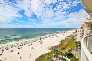 A beach view from a balcony overlooking a sandy beach with umbrellas and people.