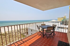 A balcony with a table and chairs overlooking a beach.