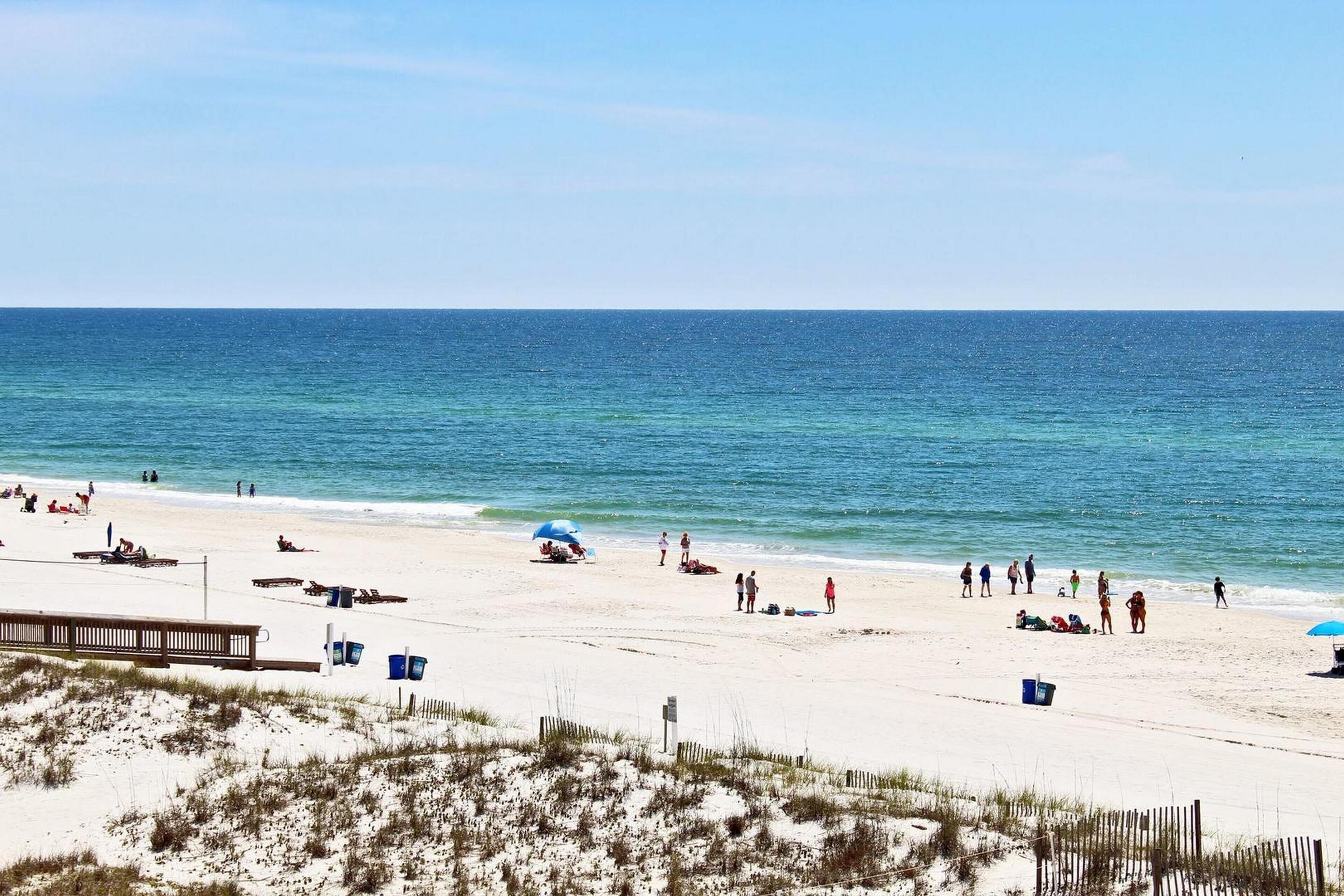 A beach with people, umbrellas, and a wooden fence.
