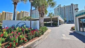 A hotel entrance with a sign, palm trees, and a parking area.