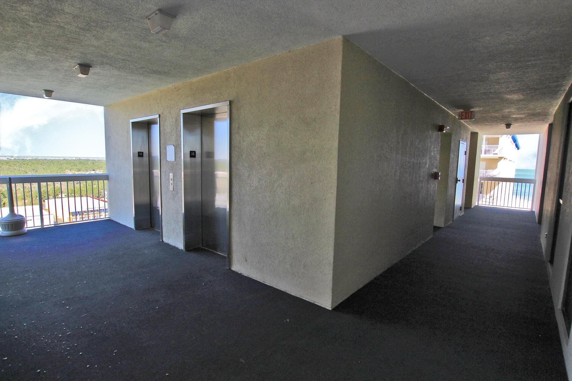 A corridor with two elevators, a concrete wall, and a balcony with a railing.