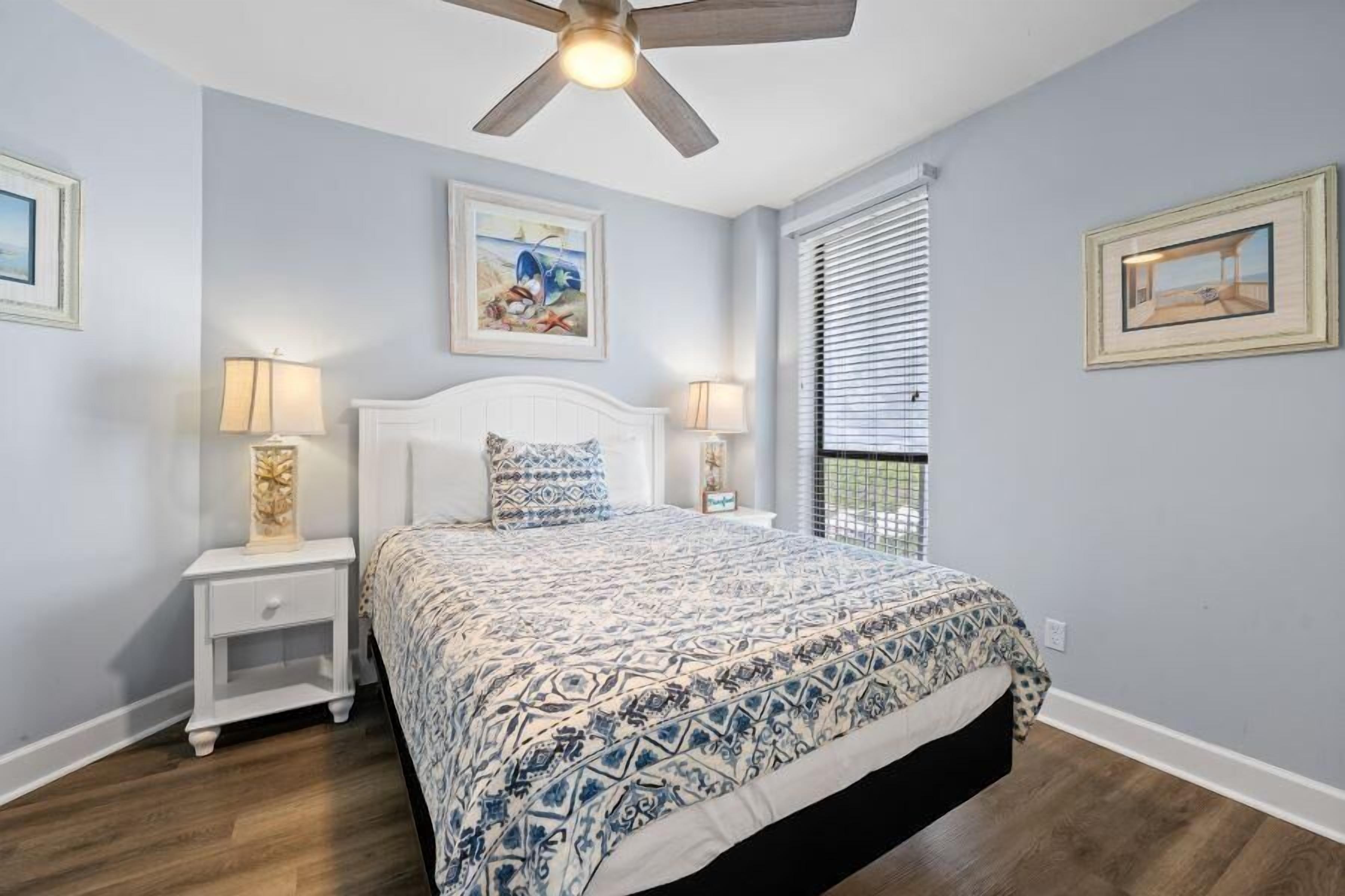 A bedroom with a bed, two nightstands, a ceiling fan, and a window with blinds.